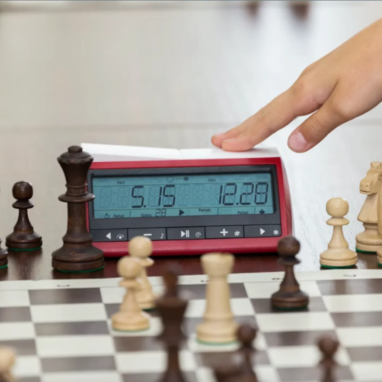 Digital chess clock with wooden chess set, mid-game with a hand adjusting the clock