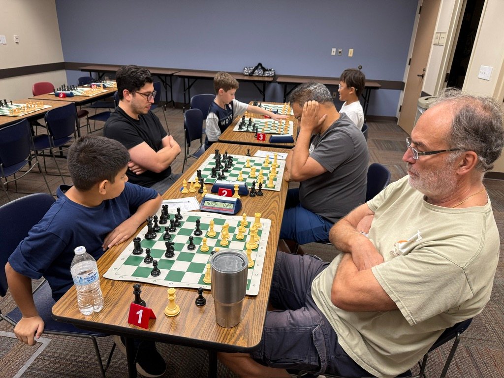 Wide view of the tournament room at Cinco Ranch Library with games in progress on three boards
